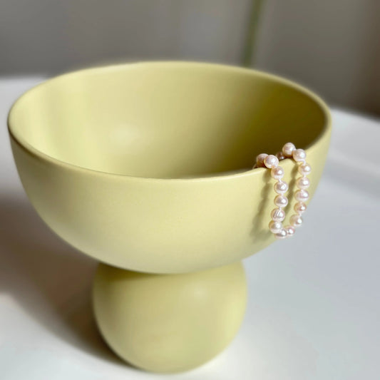 Sophie yellow ceramic vase styled with a strand of pearls draped over the rim for scale and contrast