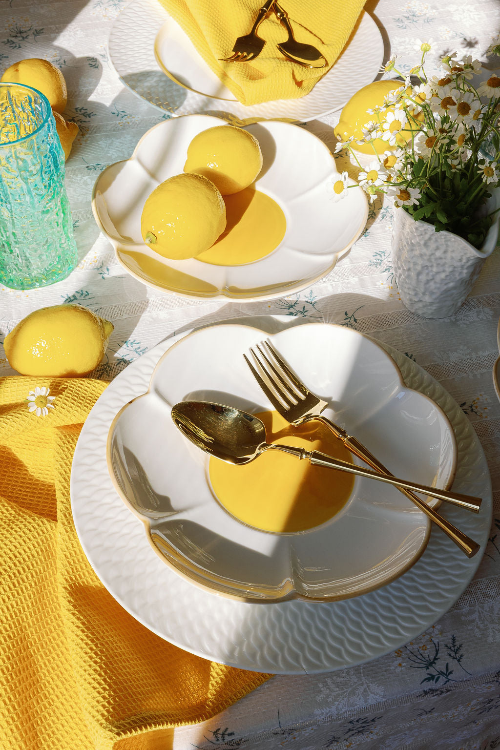 Gold fork and spoon on a scalloped white plate in a sunny lemon-themed table setting.