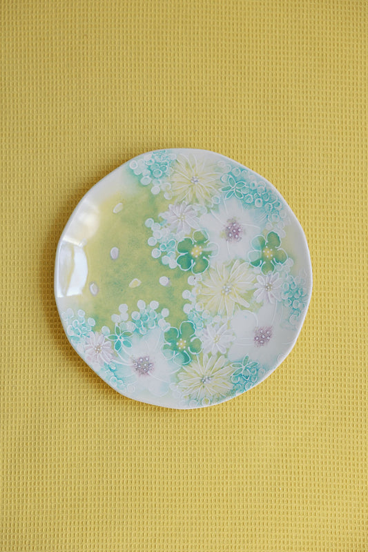 A set table with white plates featuring a blue floral pattern, accompanied by blue napkins and cutlery, with a yellow flower centerpiece on the table.