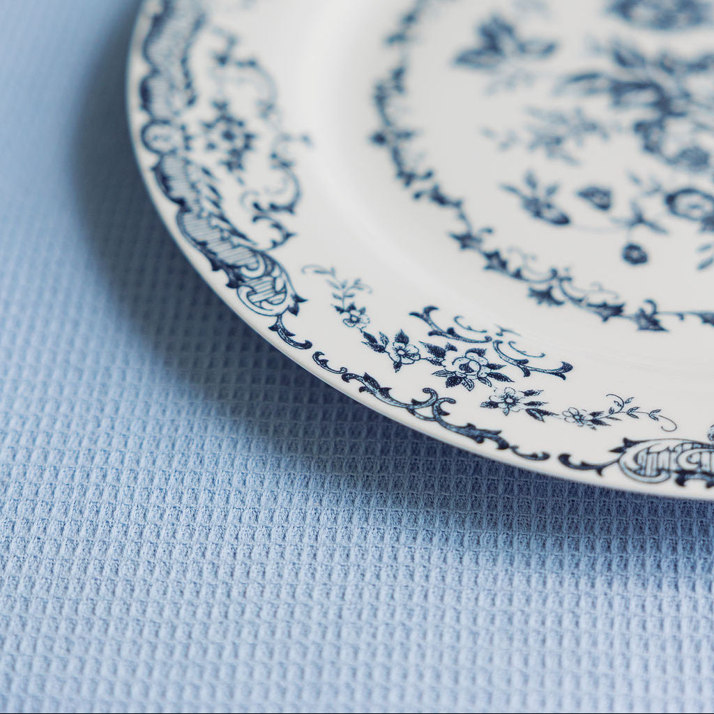 Angled view of a blue floral Chantilly Lace porcelain plate on a soft blue textured cloth.