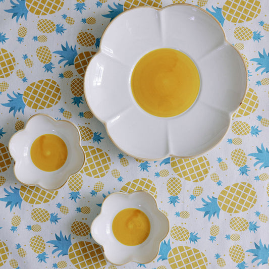 A set table with white flower-shaped plates, yellow centers, surrounded by lemons and floral tablecloth.