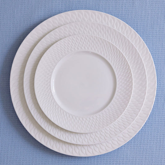 Three white ceramic plates of different sizes stacked on a textured blue surface