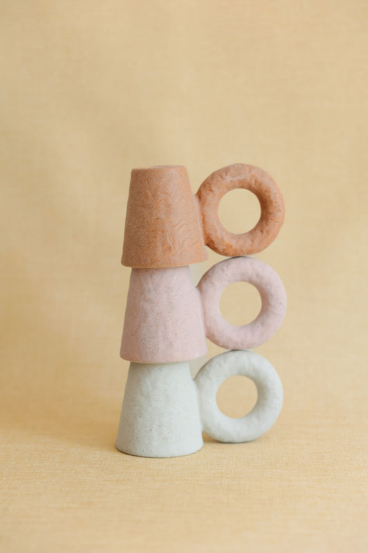 Stack of colorful ceramic candleholders on a beige background
