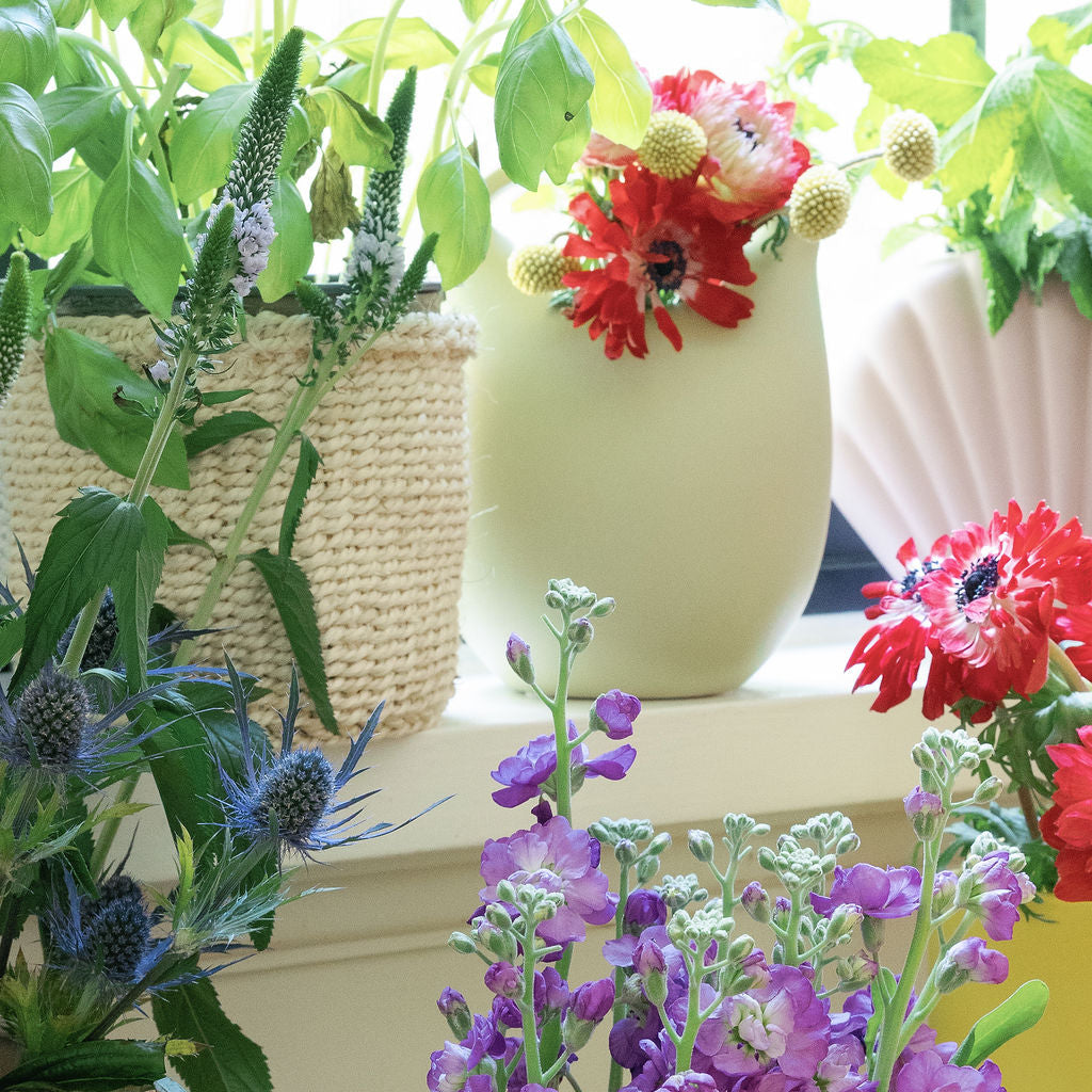 Yellow and pink ceramic basket bud vases with red poppies and purple stock, styled on a sunny windowsill.