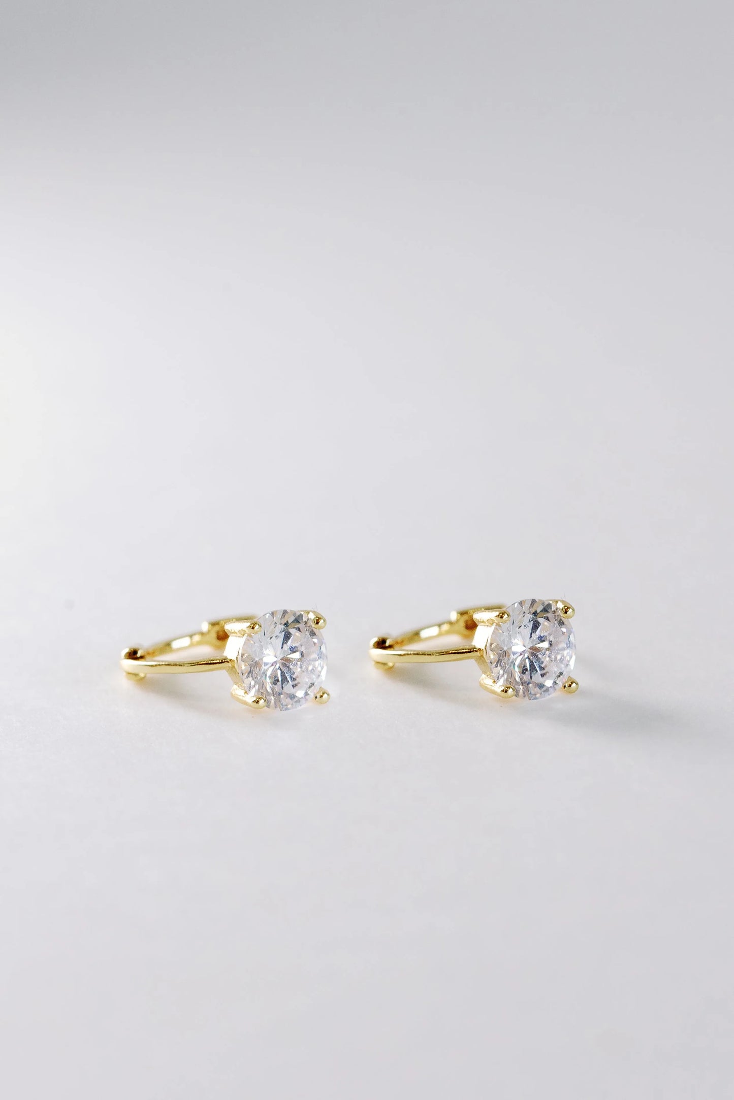 Gold crystal solitaire huggie earrings flat-lay, round prong-set stones with hinged hoops