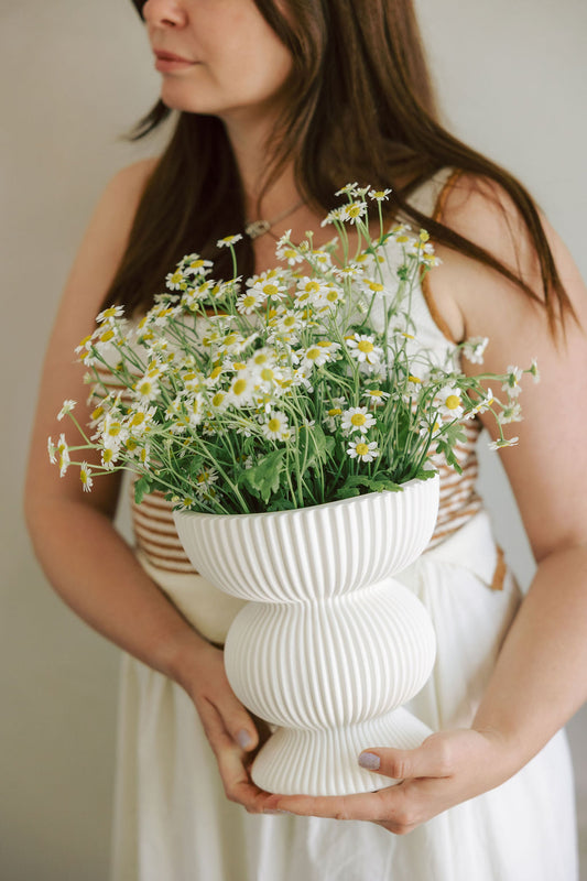 Woman holding a white vase filled with flowers against a neutral background