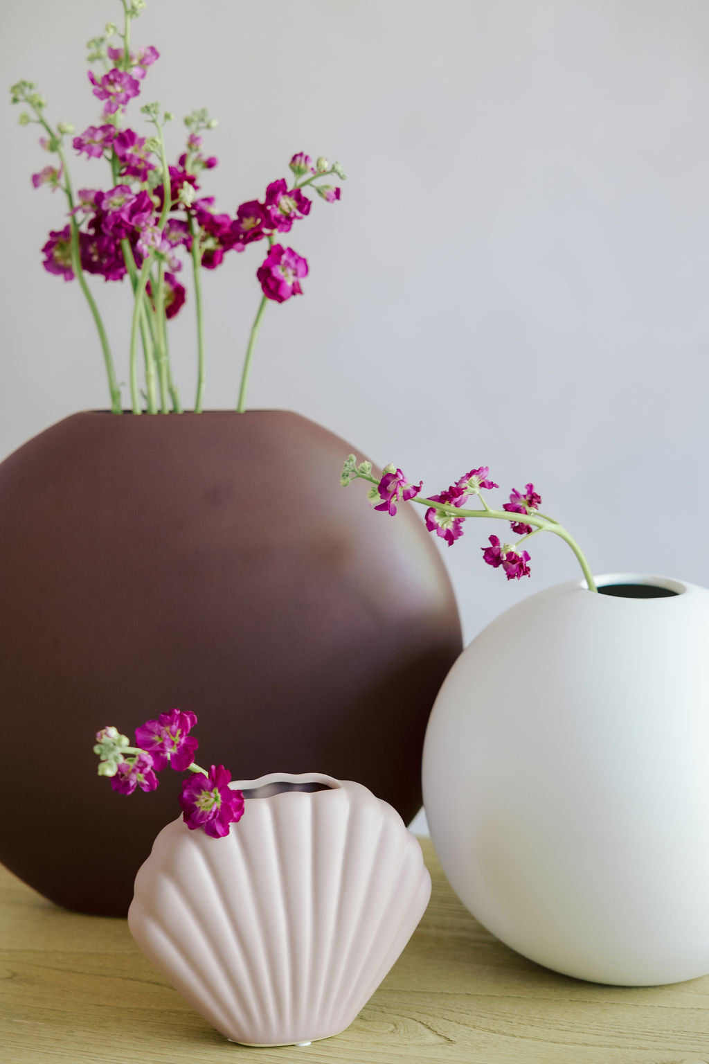 Matte white Large Orb Ceramic Vase styled with a brown vase and pink shell vase holding magenta stock flowers.
