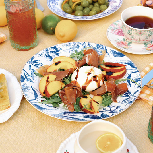 Blue and white floral porcelain plate with peach burrata salad, styled on a yellow outdoor table.