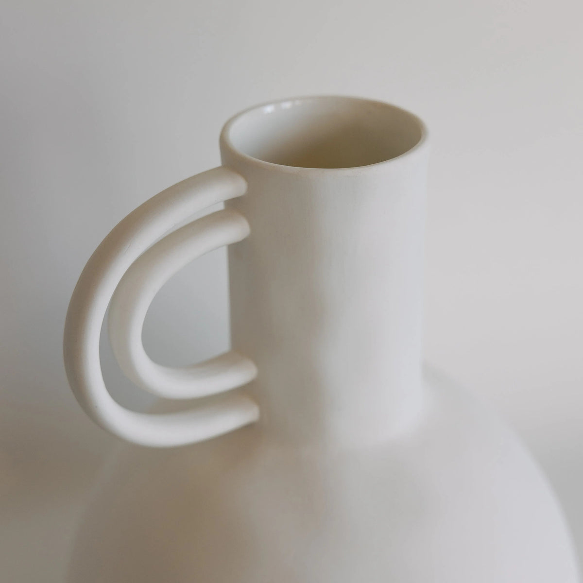 White ceramic carafe vase close-up on the open neck and sculptural double-arch handle