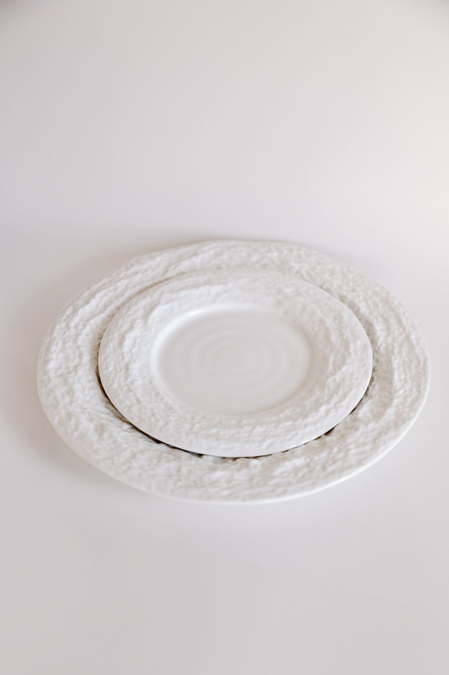 White Alpine Snow porcelain plates with craggy textured borders shown at an angle, smaller plate nested on larger.