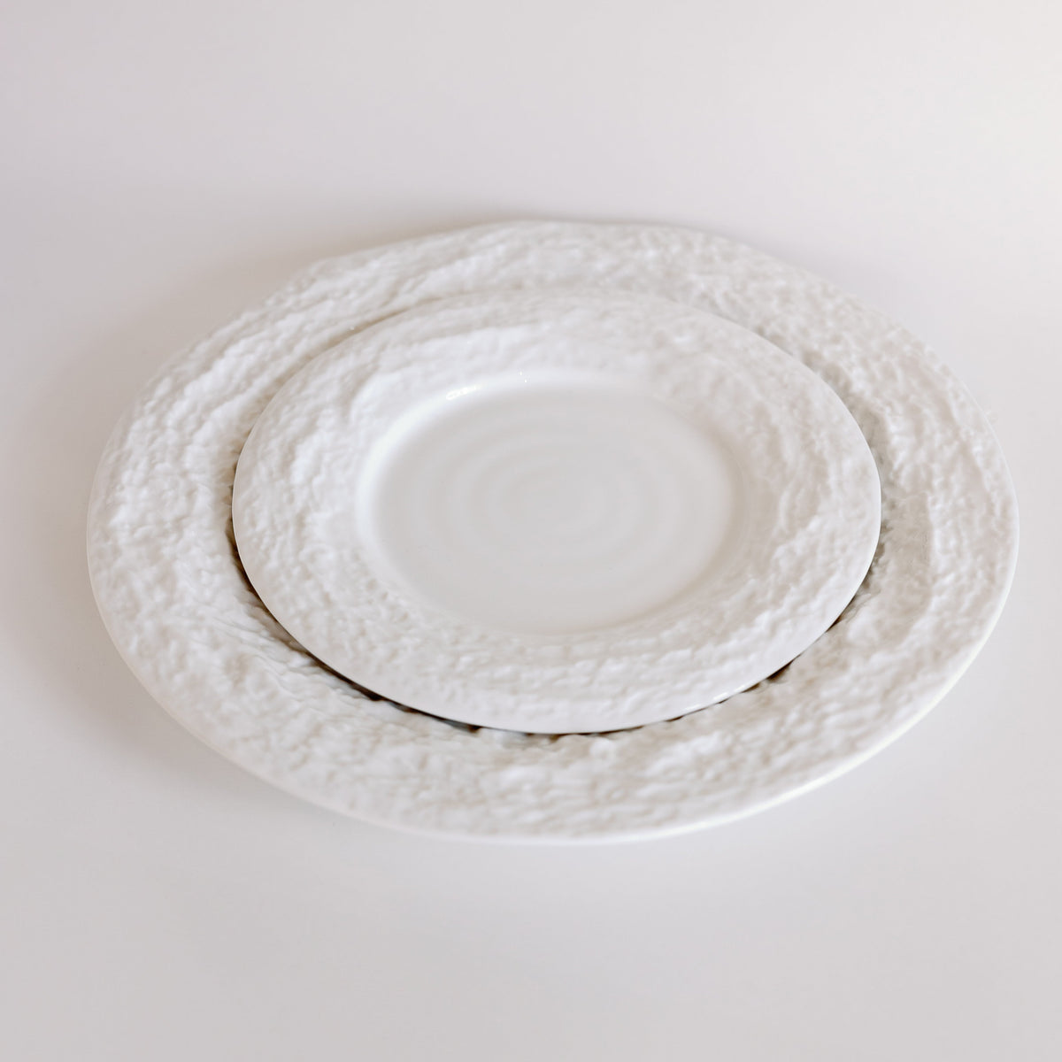 White Alpine Snow porcelain plates with craggy textured borders shown at an angle, smaller plate nested on larger.