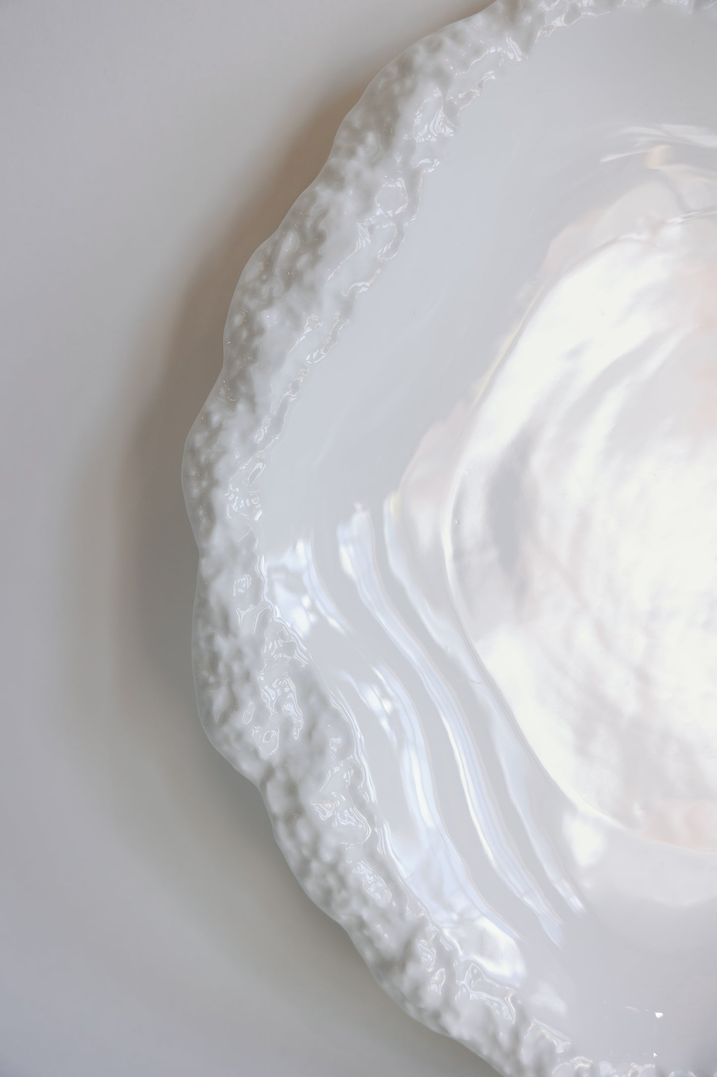 Close-up of the rough textured scalloped rim on a glossy white Amalfi porcelain plate.
