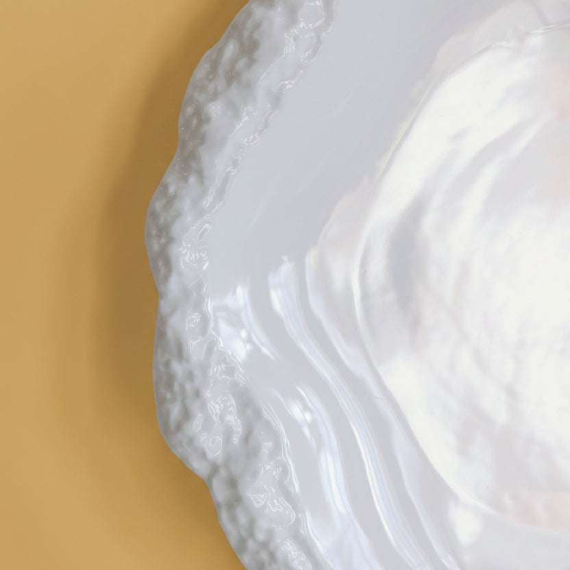 Close-up of the rough textured scalloped rim on a glossy white Amalfi porcelain plate.