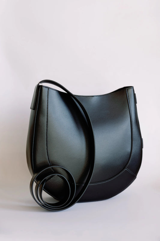 Black leather curved saddle bag, three-quarter view with coiled looped shoulder strap in front