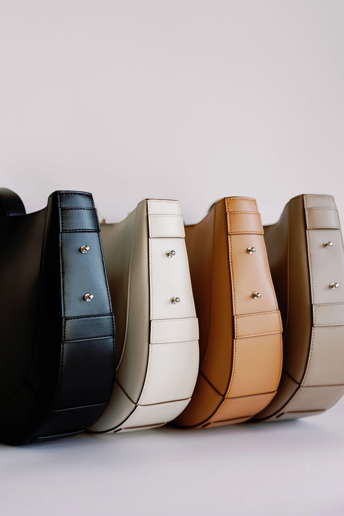 Curved saddle bags lined up in black, cream, tan and gray showing the available color range