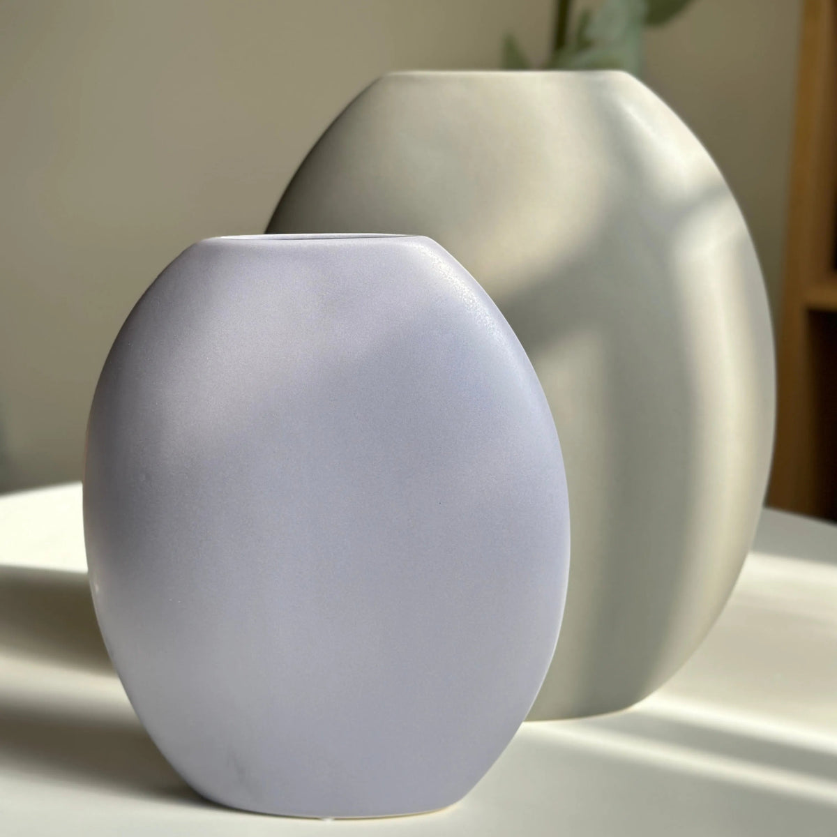 Pebble ceramic vases in lilac and cream, two pebble-shaped sizes styled on a white surface
