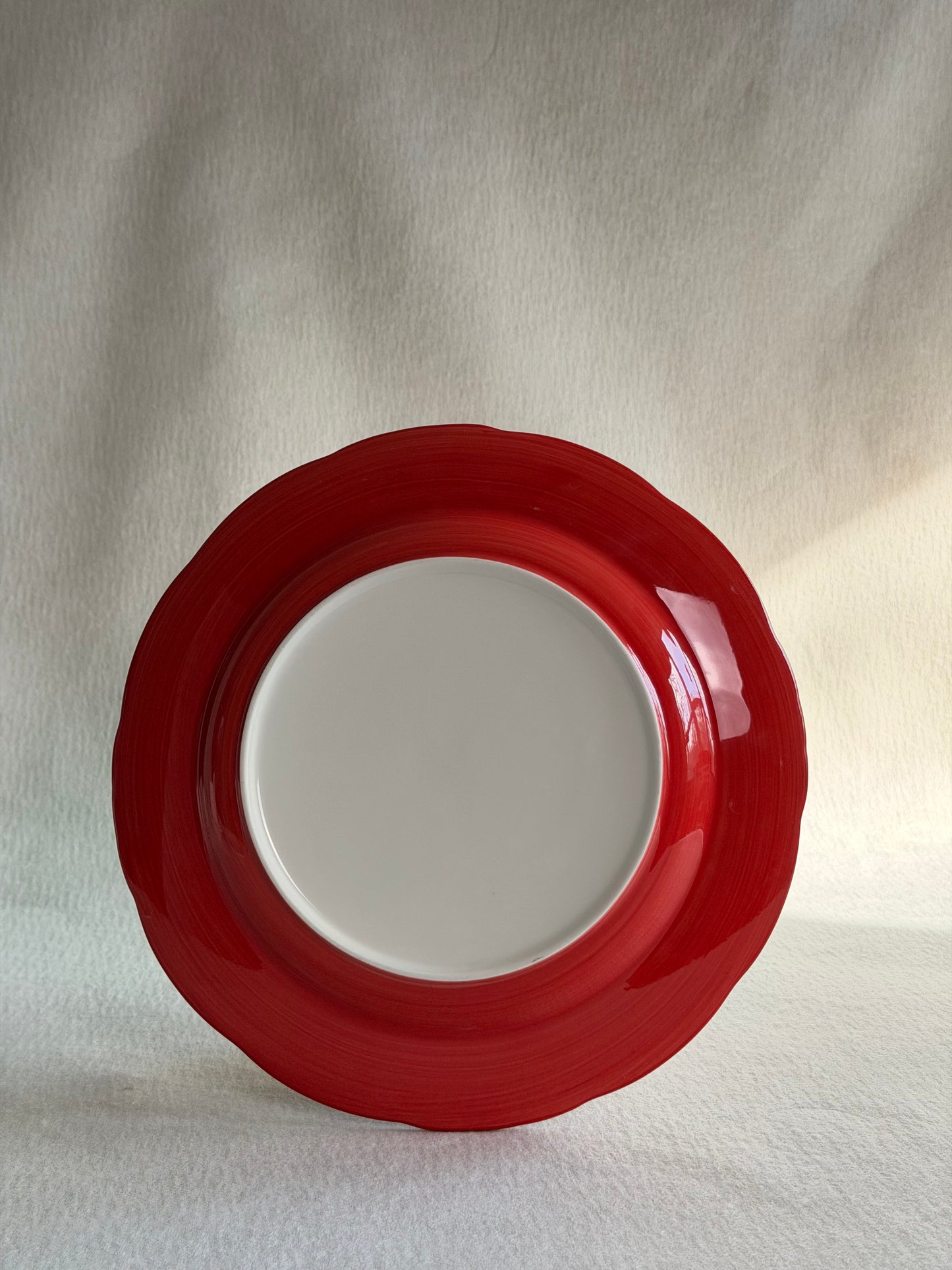 Cherry Chinoiserie porcelain plate with red painted rim and white center on soft draped fabric, full product.