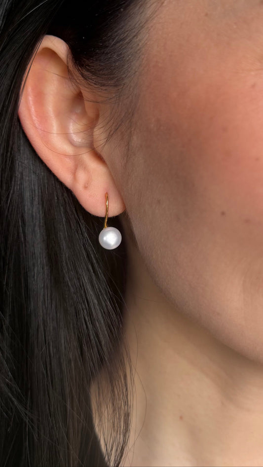 Close-up of a woman wearing a pearl drop earring with a neutral background