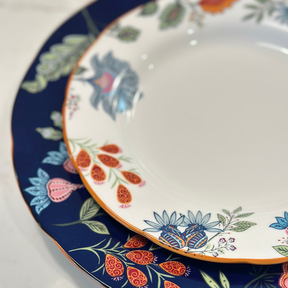 Close-up of Azure Desert floral plates with navy and orange folk flower borders and gold rims, nested in two sizes.