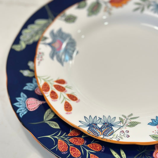 Close-up of Azure Desert floral plates with navy and orange folk flower borders and gold rims, nested in two sizes.