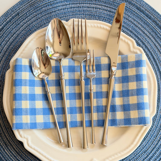 Silverware set on a blue and white checkered napkin with a blue woven placemat.
