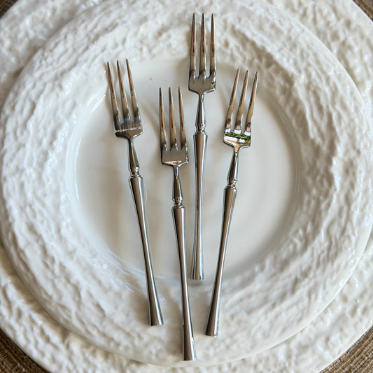 Set of silver forks on a textured white plate with a brown placemat.