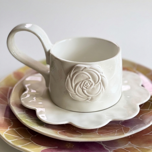 white mug with a white rose and matching white saucer on colorful plates
