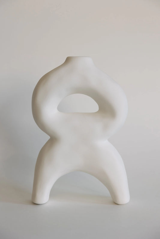White sculptural bellow bud vase, looped body with arched legs and a triangular cutout, matte ceramic front view