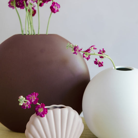 Luna Ceramic Vase in brown, rounded flat moon-shaped vase with magenta stock flowers, styled with two other vases.
