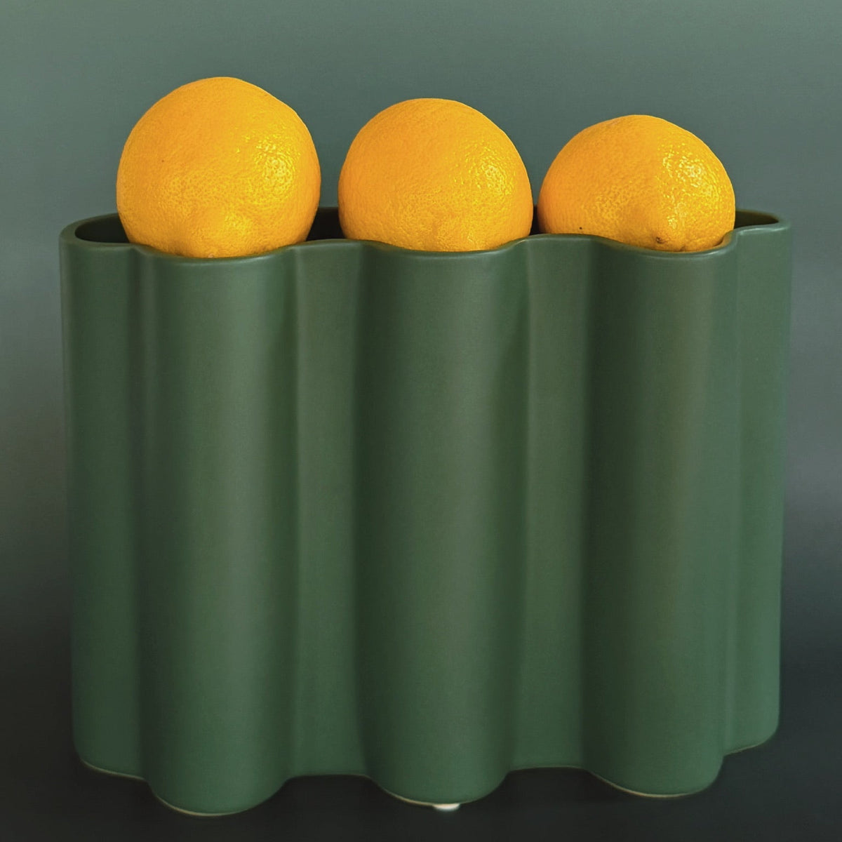 Green Ripple ceramic vase with three lemons resting on its scalloped rim against a moody gradient backdrop.