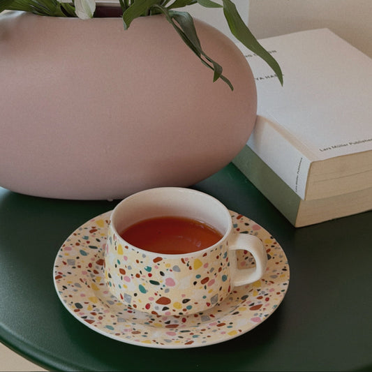 Terrazzo speckled teacup of amber tea on a matching saucer, styled beside a pink vase of white lilies.