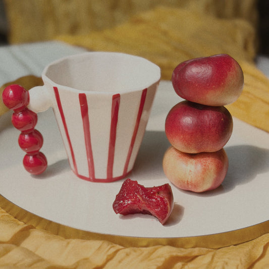 Small cup with red and white stripes, gummy bear, and small stack of apples on a yellow surface.
