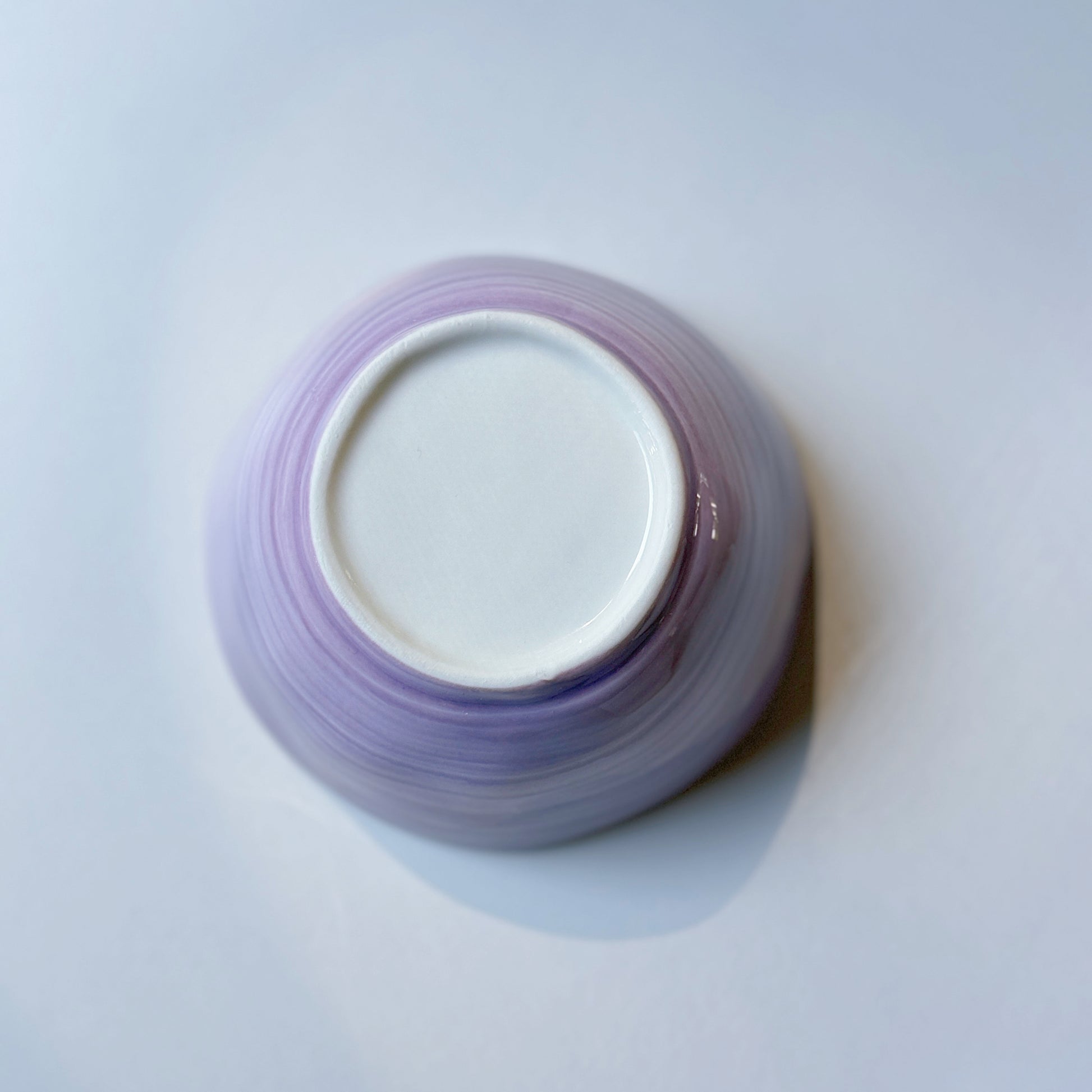 Lilac orchid porcelain bowl shown upturned, detail of brushstroke purple glaze and white footed base.