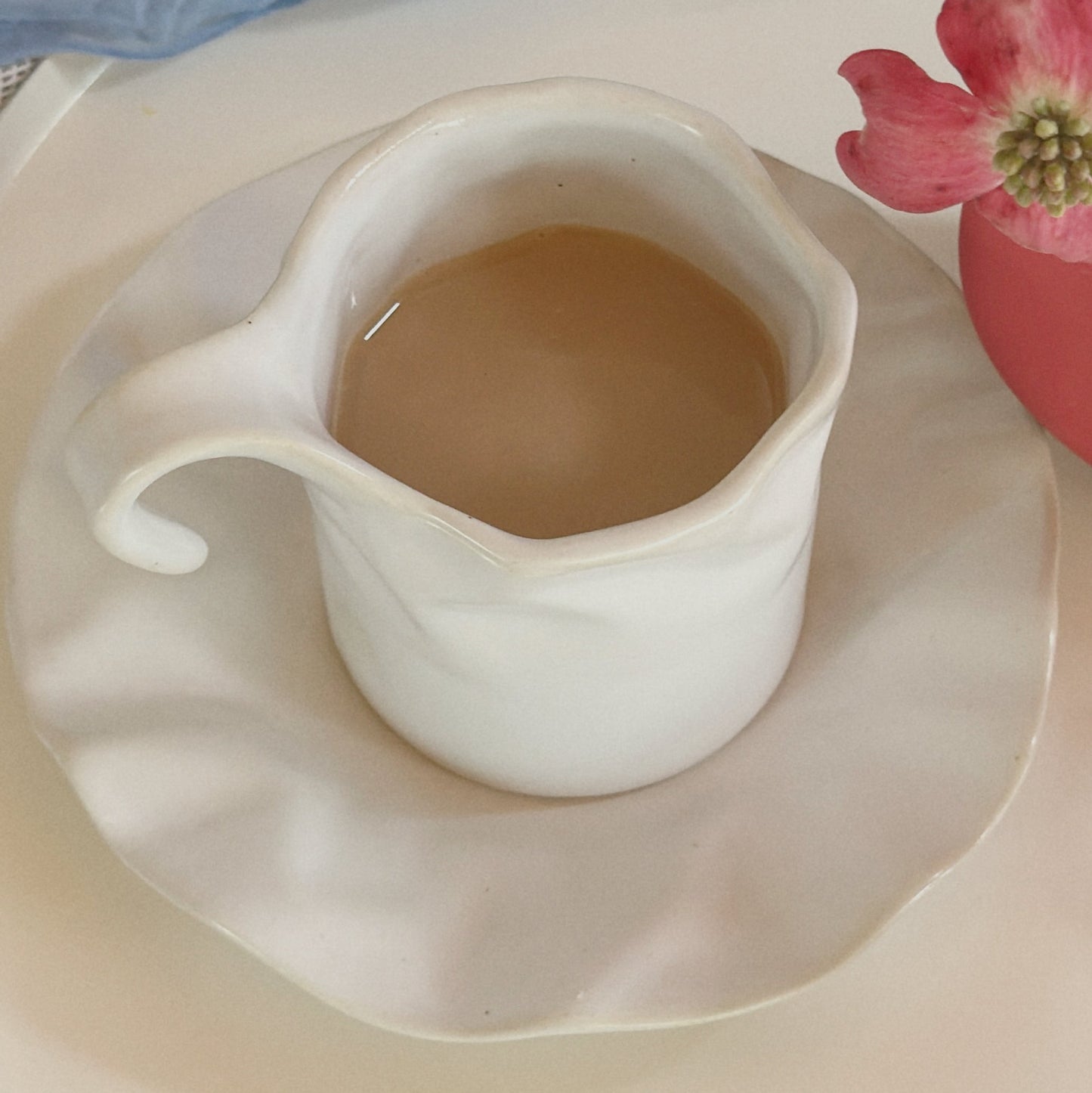 Lotus Leaf white ceramic tea cup filled with tea on its ruffled saucer, viewed from above.