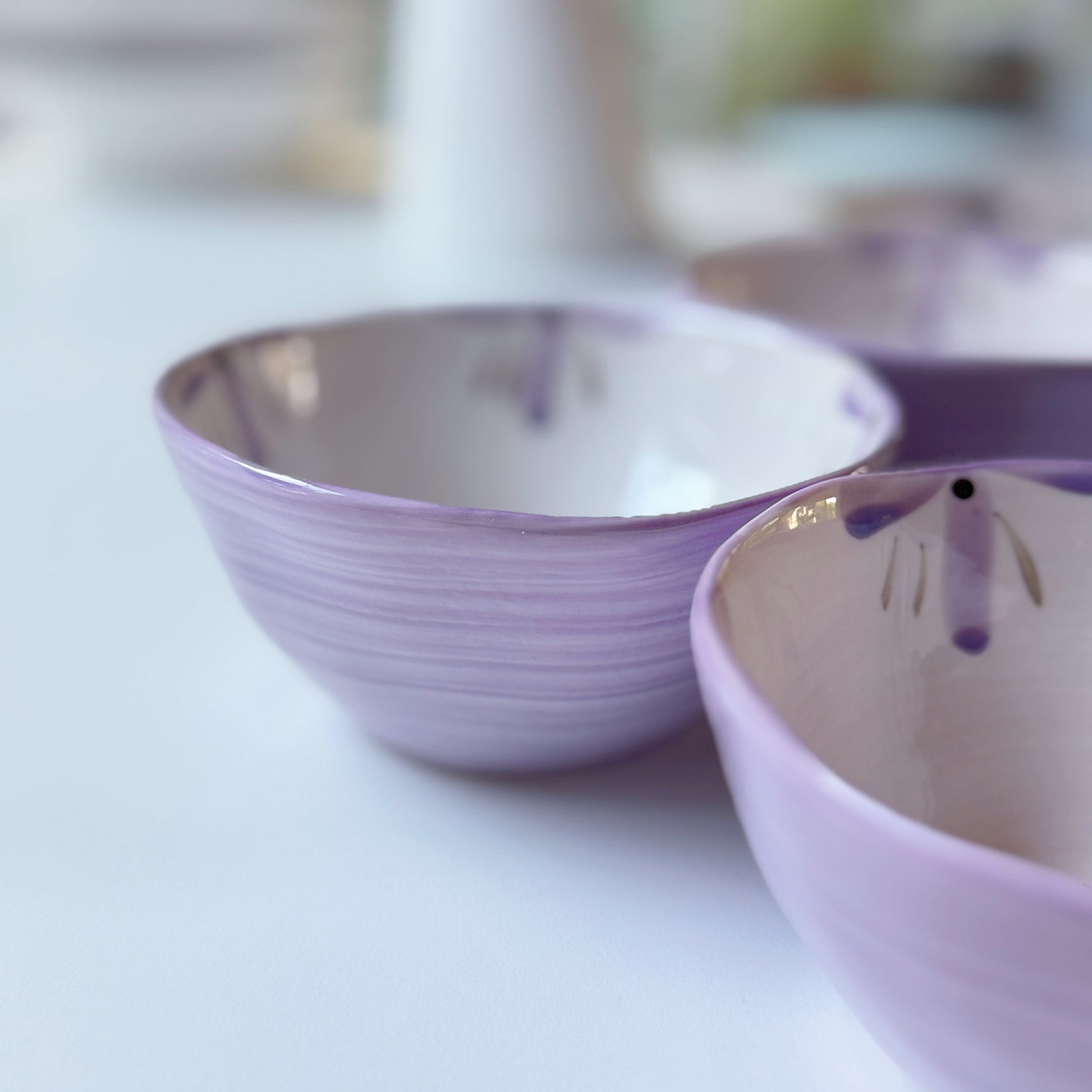Sculpted orchid porcelain dessert bowls in lilac with brushed purple petals, close-up of two angled rims.