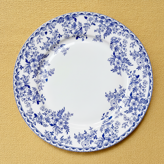 A round white ceramic plate with a blue floral border pattern, photographed from directly above on a textured mustard-yellow surface.