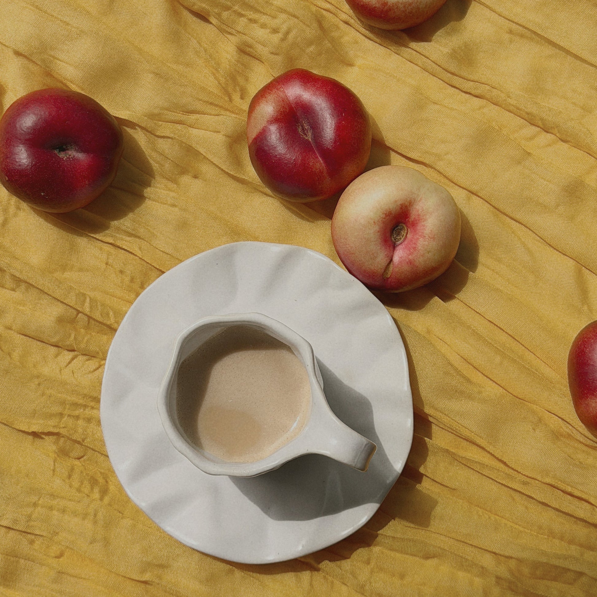 Apples and a tea cup and saucer on a yellow textured surface