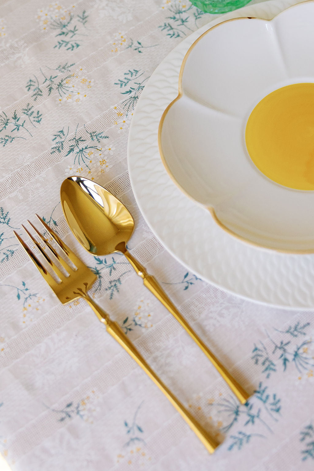 Gold fork and spoon on a floral tablecloth beside a daisy-shaped plate with yellow center.