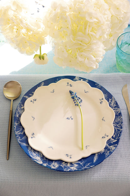 Coastal Chinoiserie dinner plate with blue floral sprigs layered on a cobalt charger, styled with gold flatware.