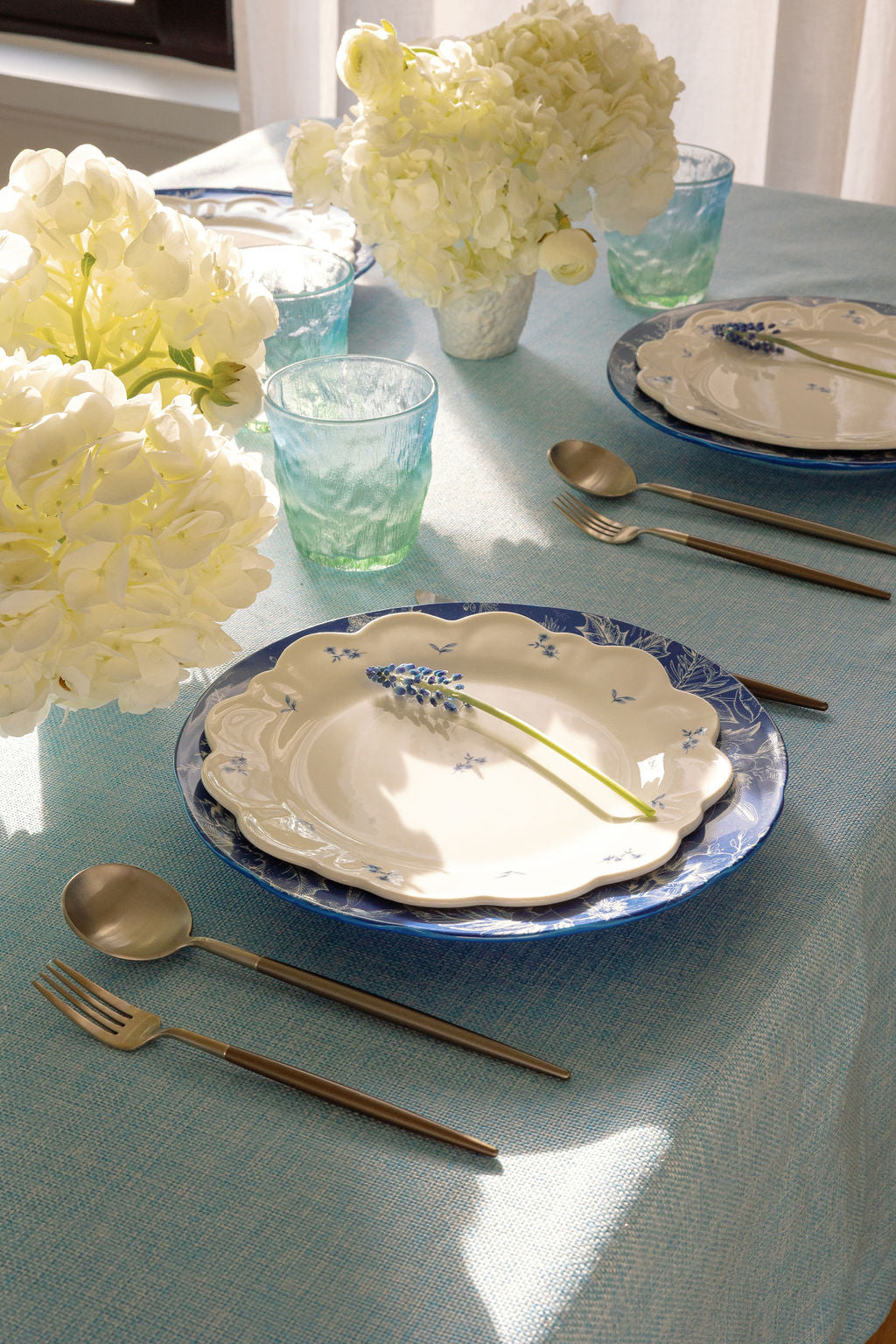 Matte silverware set styled on a blue tablecloth with floral plates and white hydrangeas.