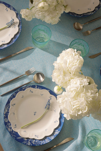 Overhead blue and white floral table setting with matte silverware, green glasses and hydrangeas.