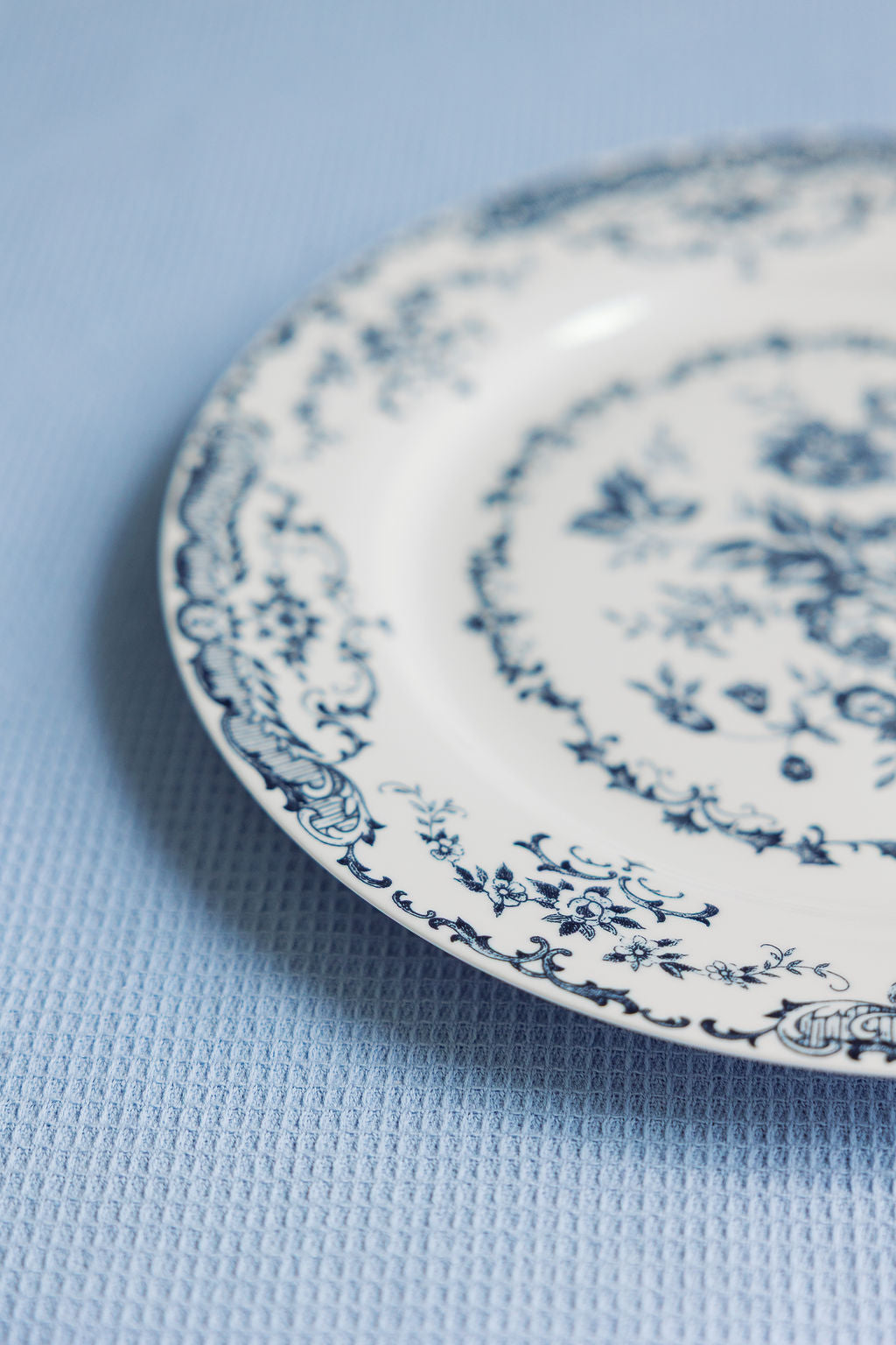 Angled view of a blue floral Chantilly Lace porcelain plate on a soft blue textured cloth.