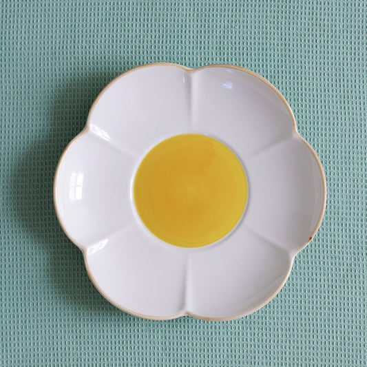 A set table with white flower-shaped plates, yellow centers, and blue glassware, surrounded by lemons and floral tablecloth.