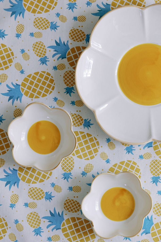 A set table with white flower-shaped plates, yellow centers, surrounded by lemons and floral tablecloth.