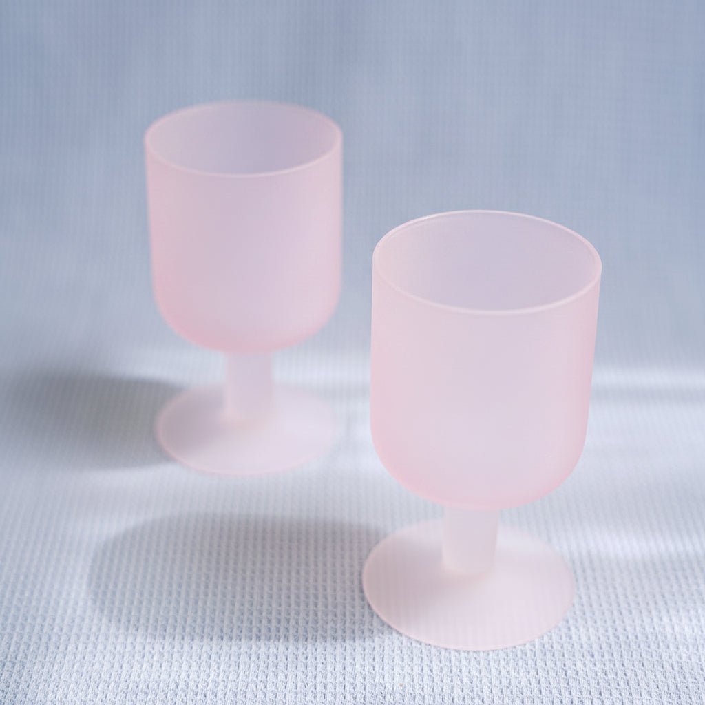 Two pink goblets with white bases on a light gray background
