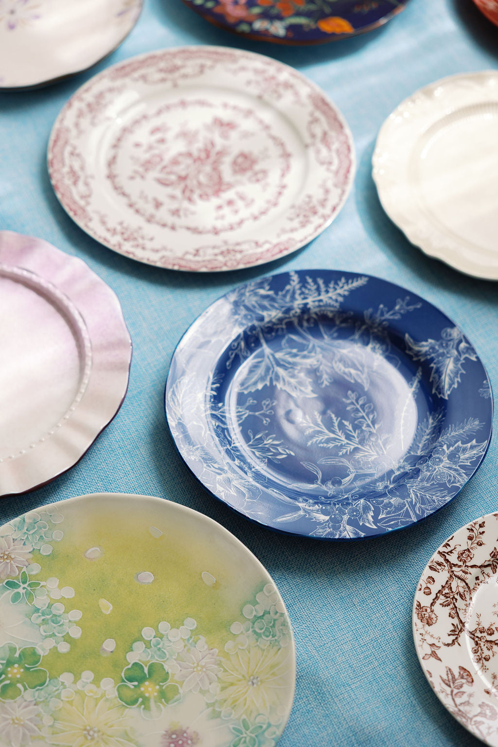 Blue and white Coastal Chinoiserie plate with fern motif among mixed vintage china on a blue cloth.