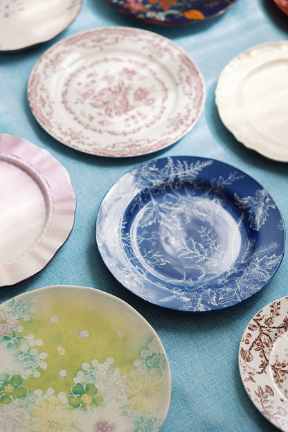 Blue and white Coastal Chinoiserie plate with fern motif among mixed vintage china on a blue cloth.