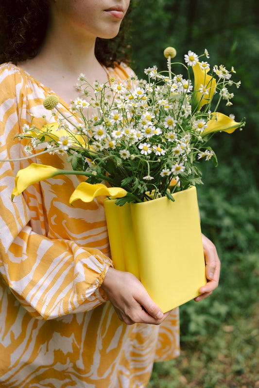 Person holding a yellow container filled with flowers against a blurred green background