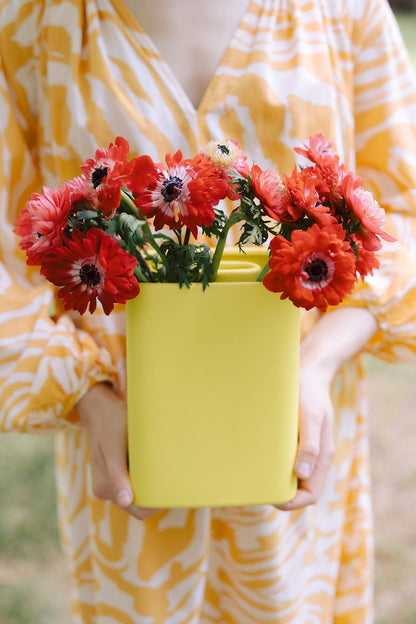 Person holds the yellow accordion ceramic vase filled with red anemones, scale shot in hand.