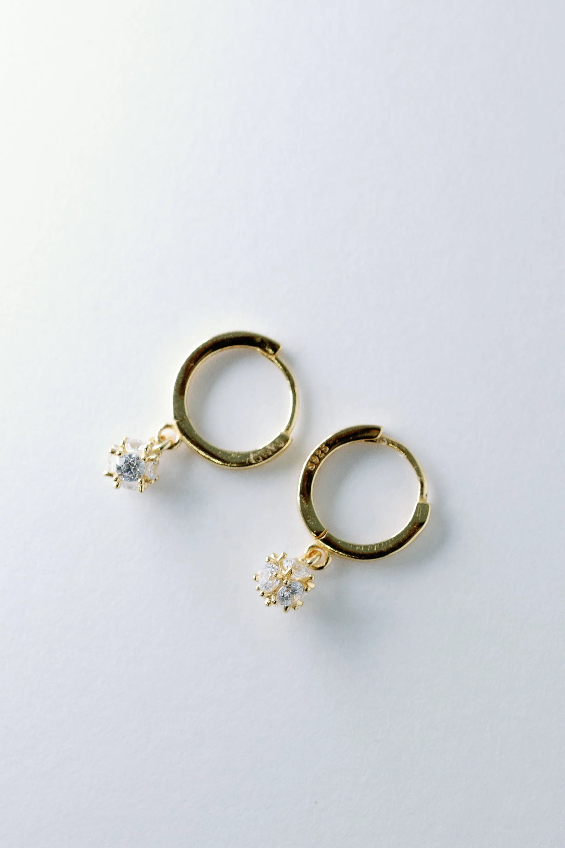 Gold crystal charm huggie earrings flat-lay, tiny prong-set crystal charms dangling from hoops